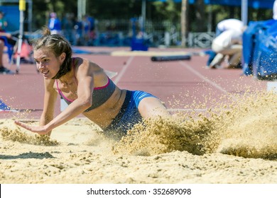 Young Woman Athlete Jumping Long Jump At Stadium. Spray Sand