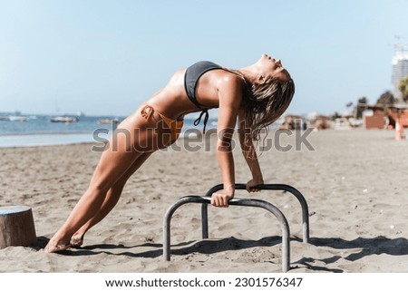 Young woman athlete stretching on parallel bars during her workout at a beach gym.