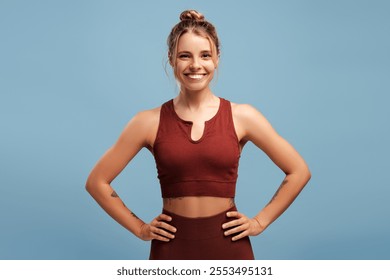 Young woman in athletic wear posing confidently holding hands on hips against blue background. Sport, health care, wellness concept - Powered by Shutterstock