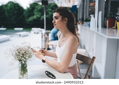 young woman in athletic wear seated at outdoor café, attentively scrolling through social media feed on smartphone app.modern lifestyle of staying connected and engaged with online communities - Powered by Shutterstock