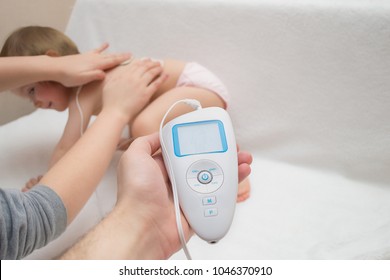 A Young Woman Attaches Electrodes From An Electrical Muscle Massager To The Body Of A Cute Beautiful Baby Girl