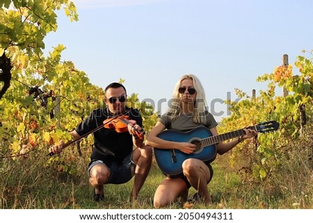 young woman and attractive man posing in vineyard. girl playing guitar and boy holding violin. pair in nature. romantic landscape. relax and mental health training. sunny autumn wallpaper. 