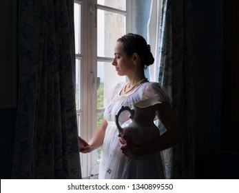 Young Woman In Authentic Regency Dress Near A Window Of A Classical Interior