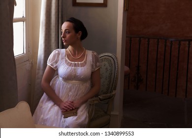 Young woman in authentic regency dress near a window of a classical interior