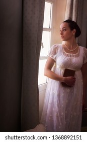 Young Woman In Authentic Regency Dress Near A Window Of A Classical Interior

