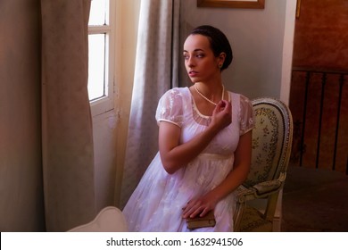 Young Woman In Authentic Regency Dress Near A Window Of A Classical Interior