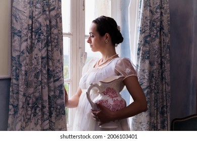 Young Woman In Authentic Regency Dress Near A Window Of A Classical Interior