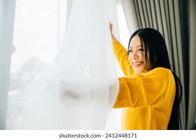 A young woman awakens early opens curtains smiles at the view feeling refreshed and happy at home. Embracing relaxation joy and morning freshness with a cheerful face. - Powered by Shutterstock