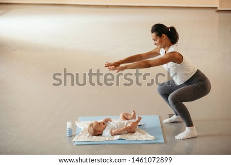 Young woman with baby practicing squats and getting in shape after the pregnancy. Copy space.