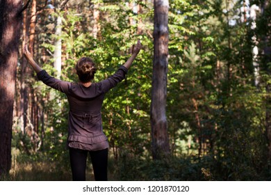 Young woman from back  arms raised up to sky, celebrating freedom. Positive human emotions feeling life perception success, peace of mind concept. Free Happy girl in summer forest enjoying nature