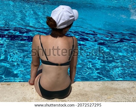 Young woman from back with victory sign gesture sits on pool.