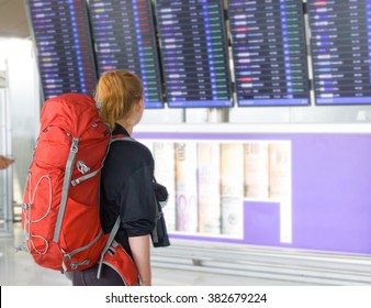 Young Woman With Backpack In Airport Near Flight Timetable