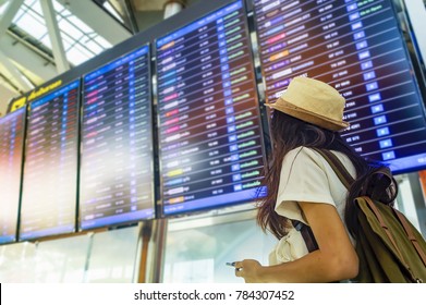 Young Woman With Backpack And Carry On Luggage In International Airport, Near Flight Information Board.Travel Concept.