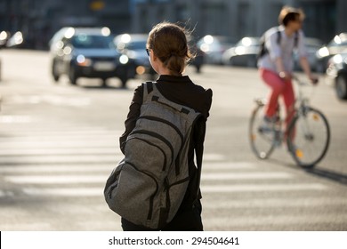 Young woman with backpack crossing the road at pedestrian crosswalk, walking in sunny European city street in summer, blurred cars and bicyclist on the background, back view - Powered by Shutterstock