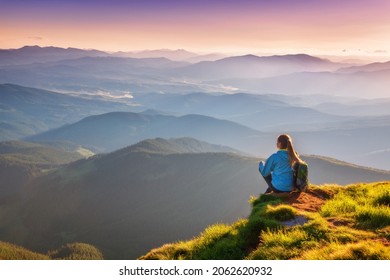 Young woman with backpack sitting on the mountain peak and beautiful mountains in fog at sunset in autumn. Landscape with sporty girl, green grass, forest, hills, sky, sunbeams in fall. Travel. Nature - Powered by Shutterstock