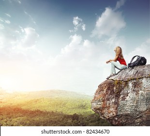 Young woman with backpack sitting on cliff's edge and looking to a sky with clouds - Powered by Shutterstock