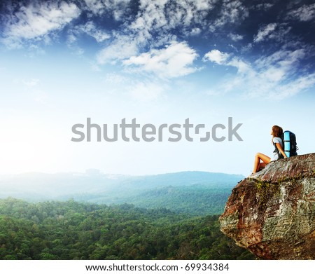 Young woman with backpack sitting on cliff and looking to a sky