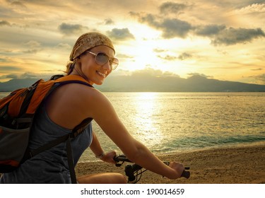 Young woman with backpack standing on the shore near his bike and smiling. - Powered by Shutterstock