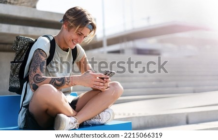Young woman with a backpack using her mobile phone while sitting on the sidewalk.