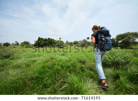 Young woman with backpack walking through a wild territory and looking to an animal.