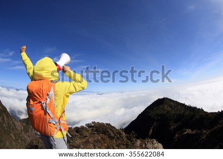 young woman backpacker shouting with loudspeaker on beautiful mountain peak