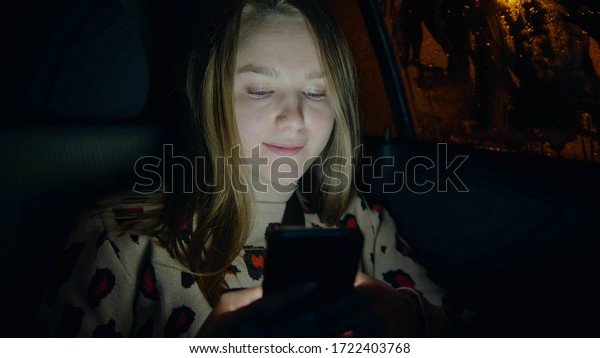 Young woman in the backseat of a car and looking at\
the phone