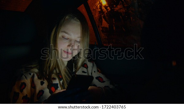 Young woman in the backseat of taxi car and looking\
at the phone