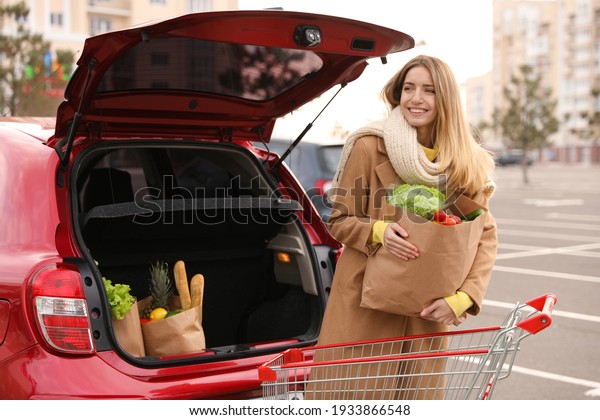 Young\
woman with bag of groceries near her car\
outdoors