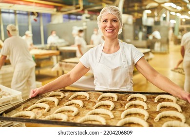 Young Woman Baker Apprentice In Factory Or Large Bakery Carries Baking Tray With Croissants