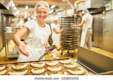 Young woman as a baker apprentice in the large bakery sprinkles poppy seeds on croissants - Powered by Shutterstock