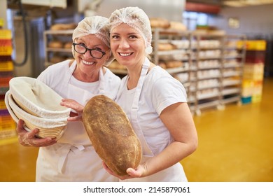 Young Woman Baker Apprentice And Senior Baker With A Loaf Of Bread In A Large Bakery