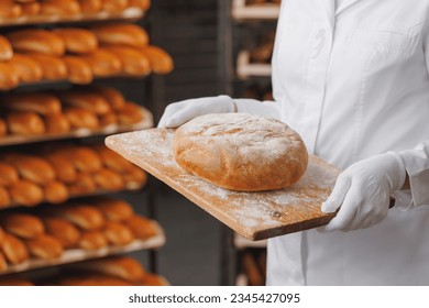 Young woman baker in chef uniform holding freshly craft baked bread. Industrial food production. - Powered by Shutterstock