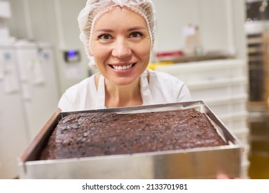 Young Woman Baker Trainee Proudly Shows A Fresh Chocolate Cake In The Bakery