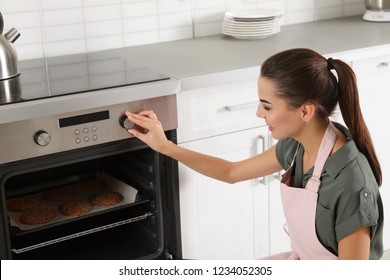 Young Woman Baking Cookies In Oven At Home