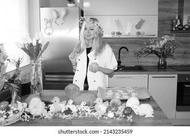 Young Woman Baking Easter Cakes In Decorated Kitchen. Celebrating Spring Holidays In 2022. Girl Wearing Chef Uniform And Flower Wreath On Head. Chicken And Rabbit Or Bunny Shapes. Big Gingerbread Lamb