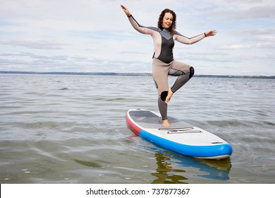 Young woman balances on one leg on inflatable SUP board on water.