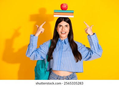 Young woman balancing books on her head in front of a vibrant yellow background - Powered by Shutterstock