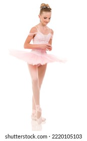 Young woman ballerina in white tutu, dancing on pointe with arms overhead, in the studio against a dark background. High quality photo