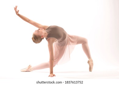 Young woman ballet dancer in pointe shoes wearing a brown leotard and pink skirt, kneeling while dancing floor work in the studio against a white background.