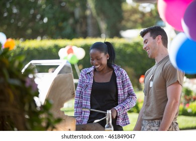 Young Woman Barbecuing With Male Soldier At Homecoming Party