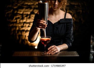 Young Woman Bartender At Dark Bar Holds Steel Foam Blower Over Glass With Alcoholic Cocktail.