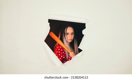 Young woman with baseball bat in hole of white background. Pretty lady with bat