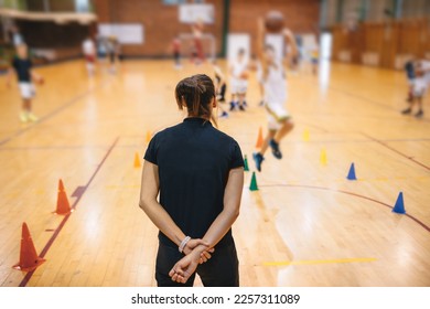 Young woman basketball coach coaching grpup of school junior basketball players. Kids having fun at basketball training session - Powered by Shutterstock