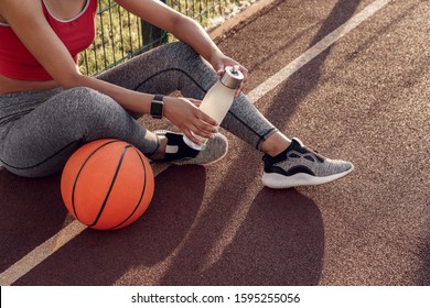 Young woman basketball player sitting on ground with ball outdoors holding bottle of water rest close-up - Powered by Shutterstock