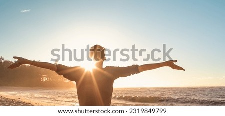 Young woman basks in sunsets warm rays of sunshine with outstretched arms.