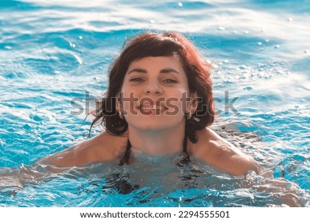 Young woman bathes blue water of the pool, close-up.