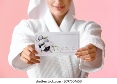 Young Woman In Bathrobe With Gift Voucher On Pink Background, Closeup