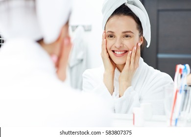 Young woman in bathrobe looking in bathroom mirror