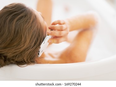 Young woman in bathtub talking cell phone. rear view - Powered by Shutterstock