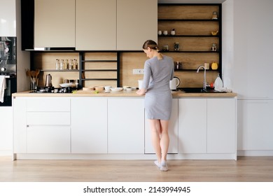 Young woman with beautiful body standing next to a modern kitchen while cooking. Back view - Powered by Shutterstock